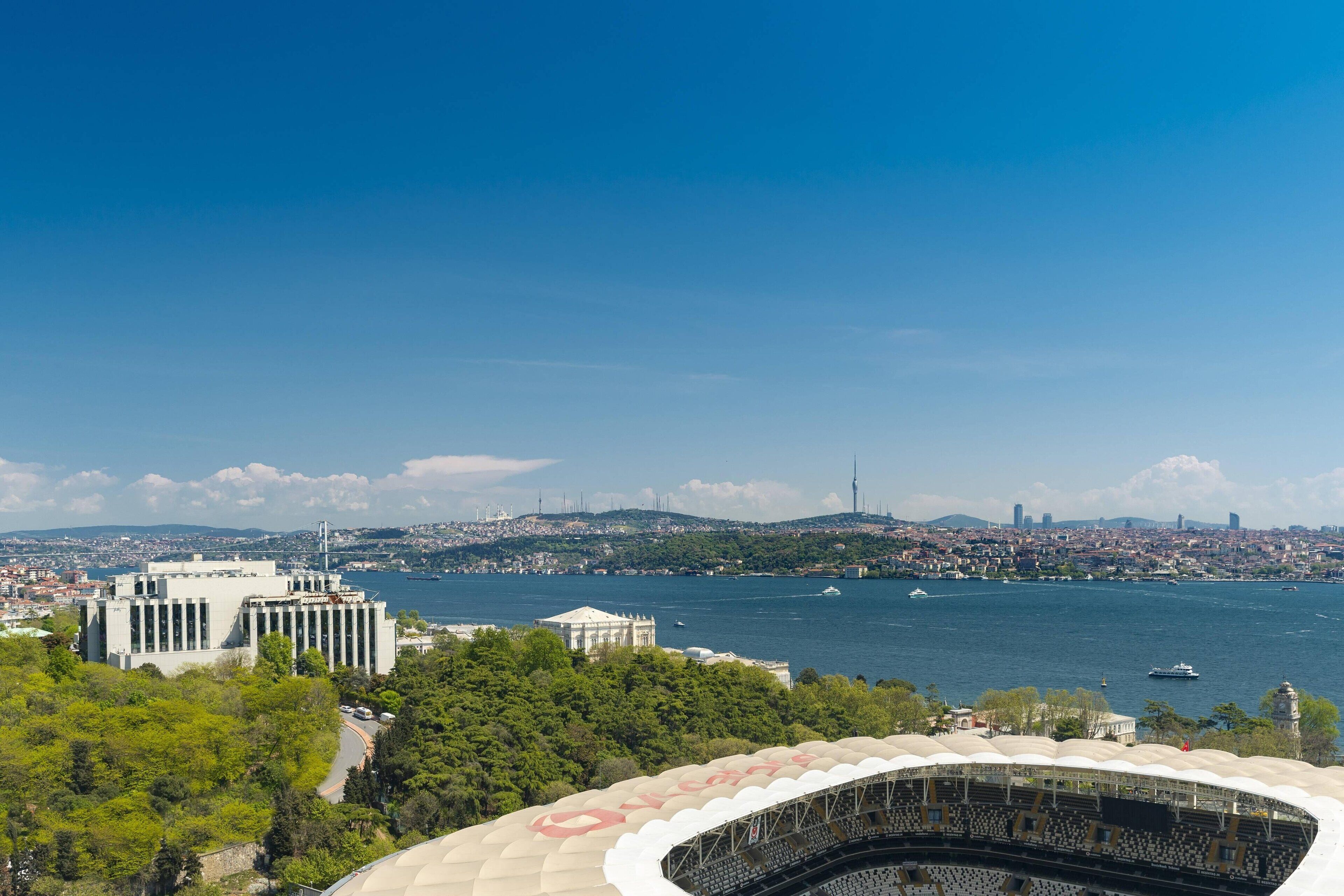 Um estádio com uma área de assentos ampla e aberta, e vista para uma paisagem urbana que inclui um corpo de água e edifícios ao fundo.