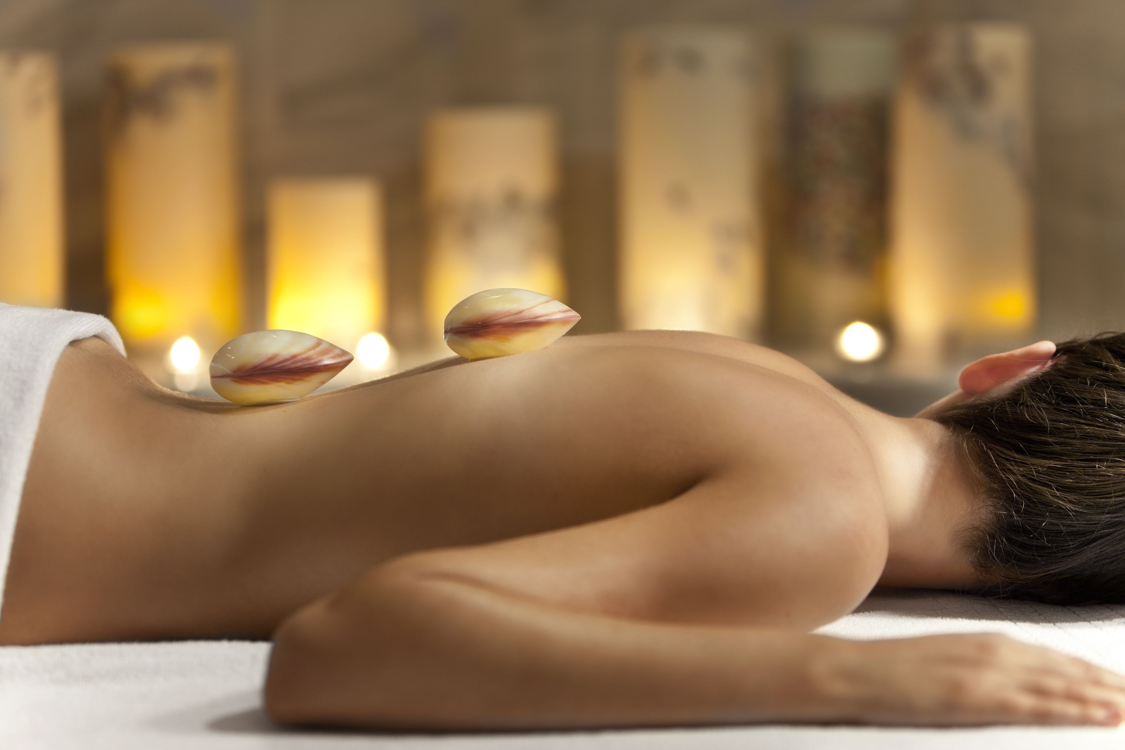 Iemand ontvangt een massage met kaarsen in een zwak verlichte ruimte.