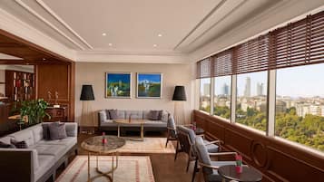 A spacious living room with a sofa, chairs, a coffee table, and a view of the city through large windows.