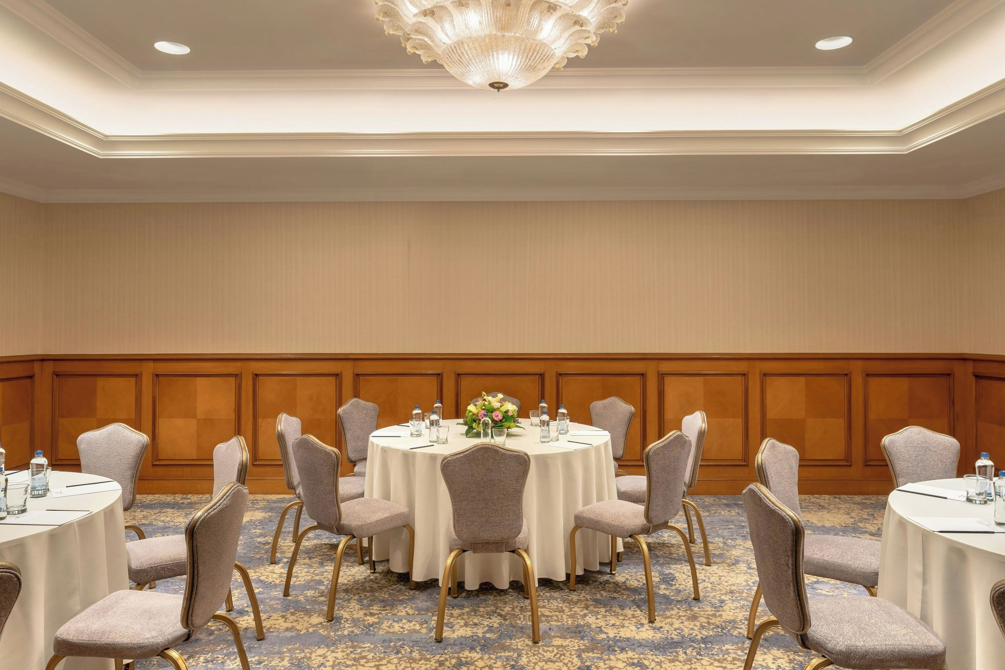A conference room with round tables, chairs, and a chandelier.