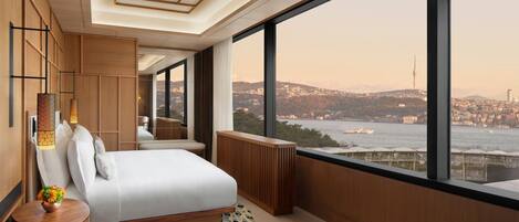 A modern hotel room with a large window, a bed, a bedside table, and a view of a cityscape and water.