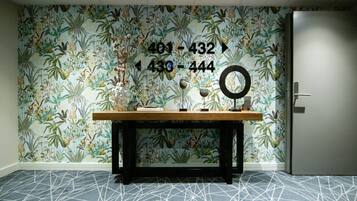 A room with a floral wallpaper, a wooden table with books and a mirror, and a geometric patterned carpet.