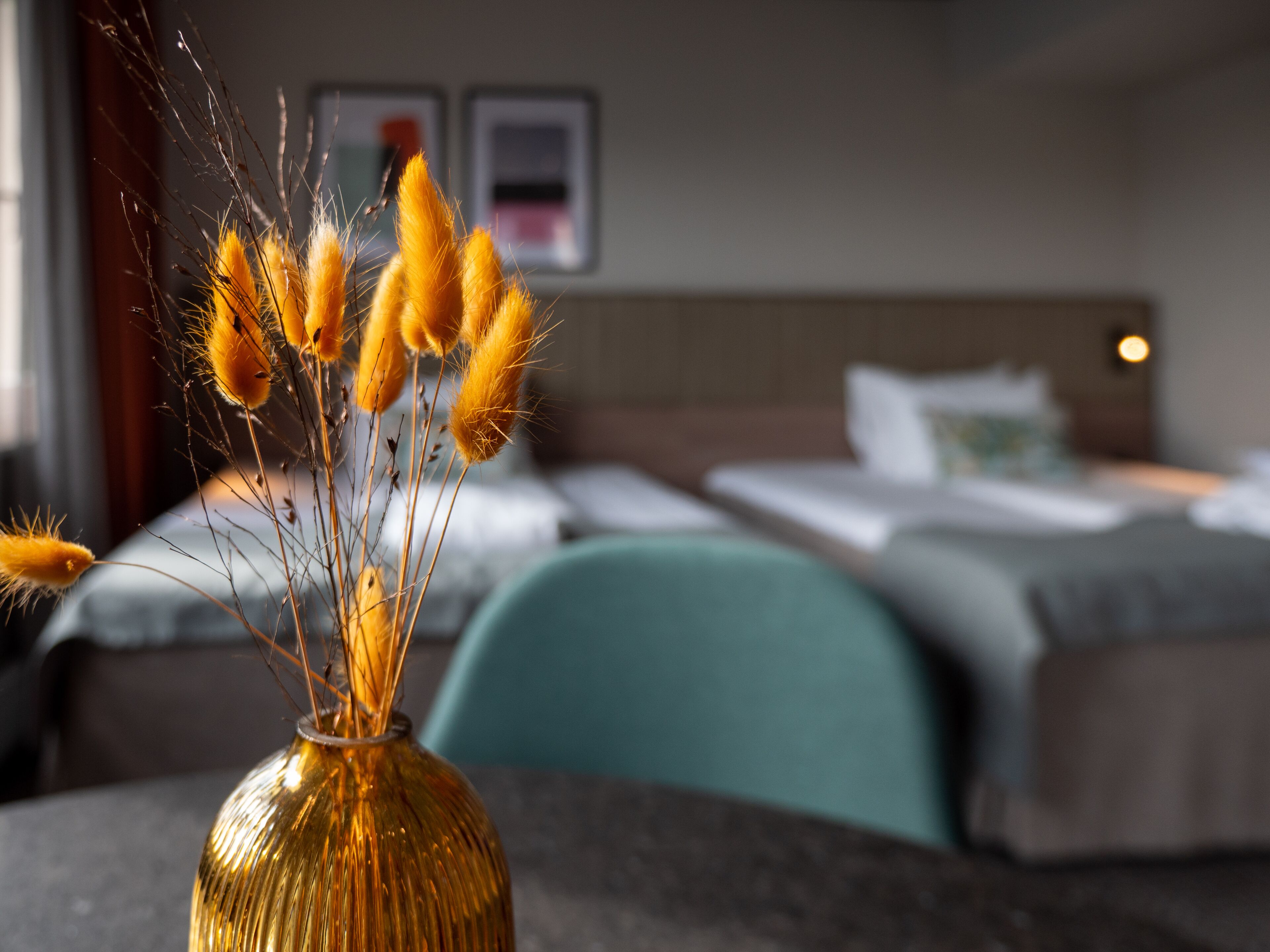 Habitación de hotel con cama, mesita de noche con un jarrón de flores amarillas y vista al interior de la habitación.