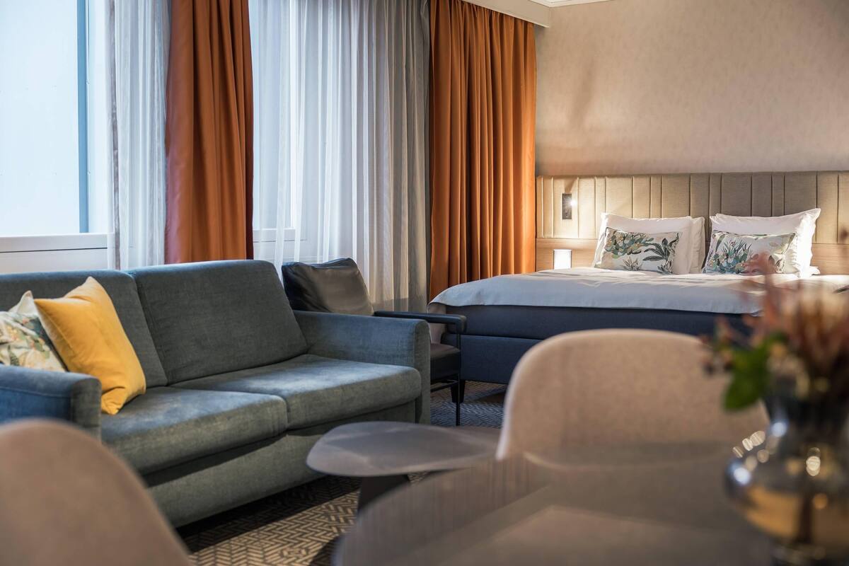 A hotel room with a bed, a sofa, a chair, and a small table.