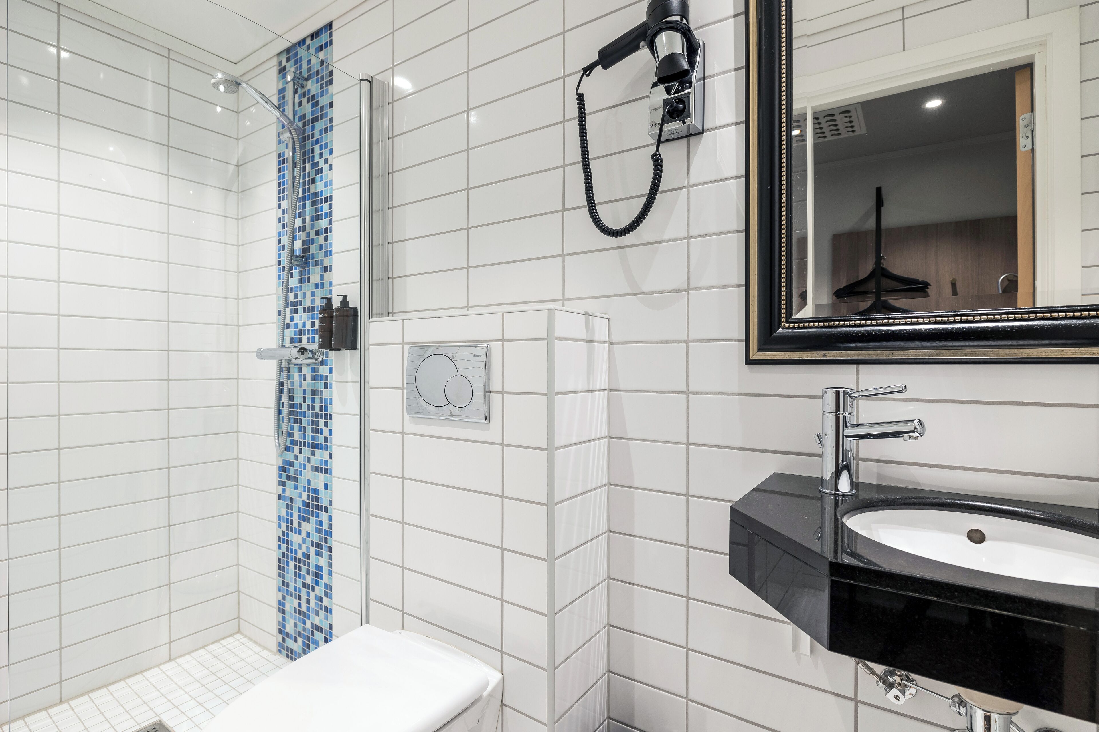 Un baño moderno con paredes de azulejos blancos, una ducha con mosaicos azules, un lavamanos negro y un espejo con marco negro.