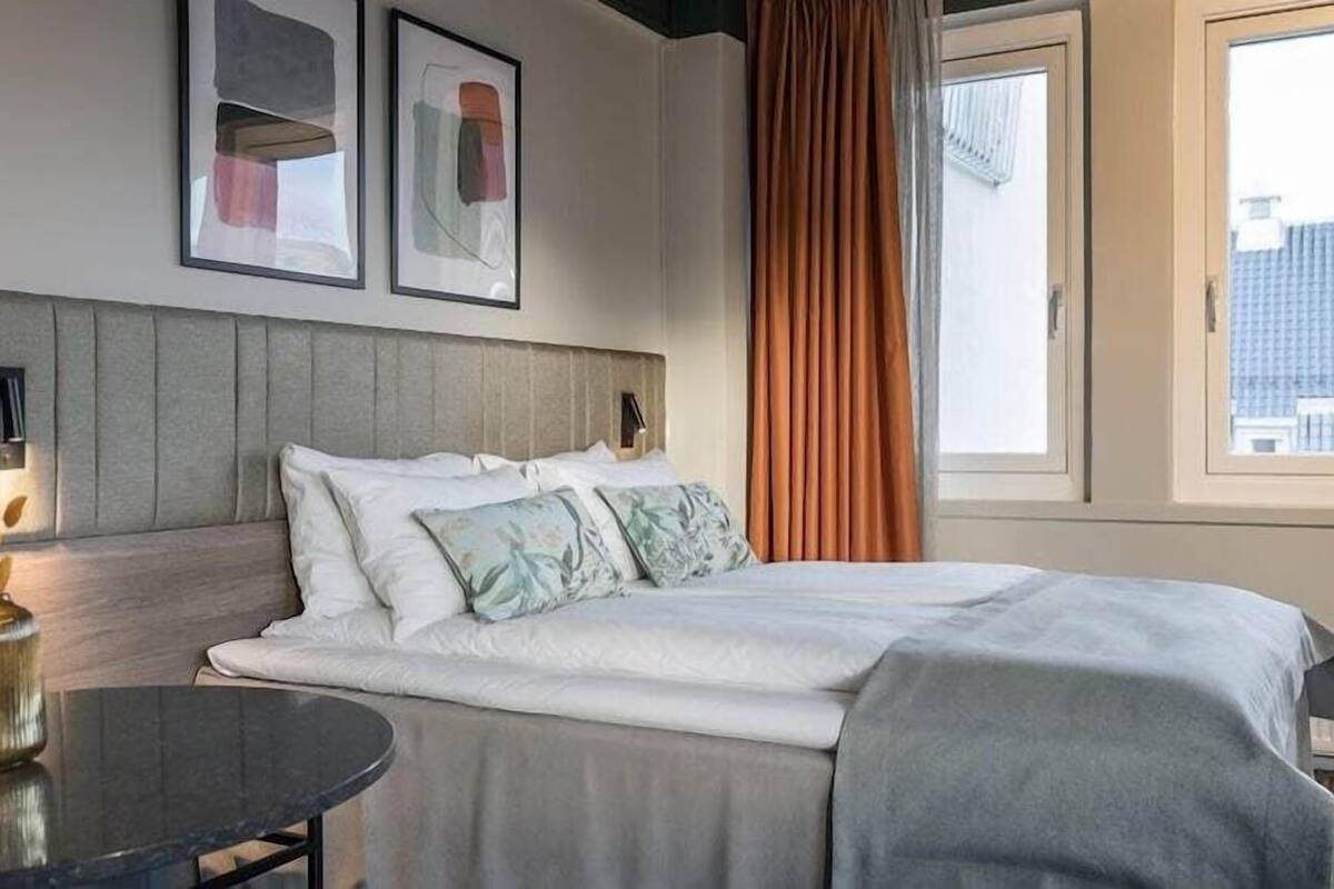 A hotel room with a bed, a round table, and a window with a view of buildings.