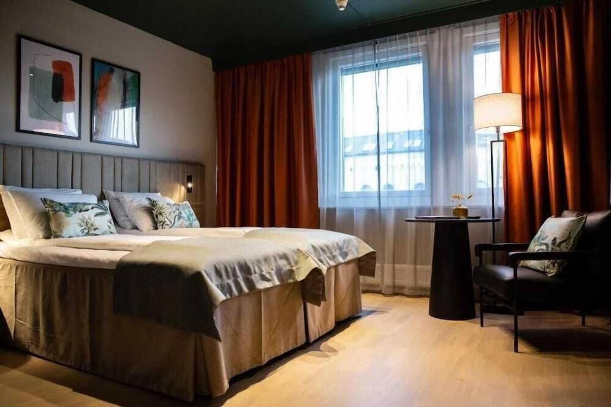 A hotel room with a bed, a chair, a table, and a window with curtains.