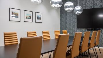 A conference room with a long table, multiple chairs, framed pictures on the wall, a large flat-screen TV, and hanging spherical light fixtures.