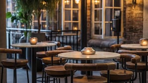 A cozy restaurant interior with round tables and leather chairs, featuring a rustic brick wall and warm lighting. - Quality Hotel Prinsen (Trondheim)