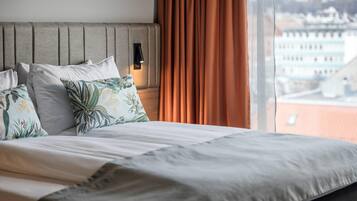 Une chambre d’hôtel avec un lit, une tête de lit, une fenêtre avec des rideaux et une vue sur les bâtiments environnants.