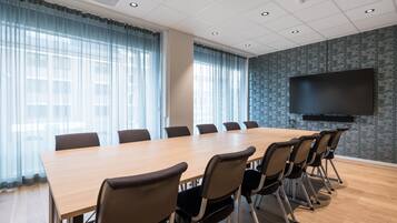 A conference room with a long table, chairs, a flat-screen TV, and large windows with curtains.
