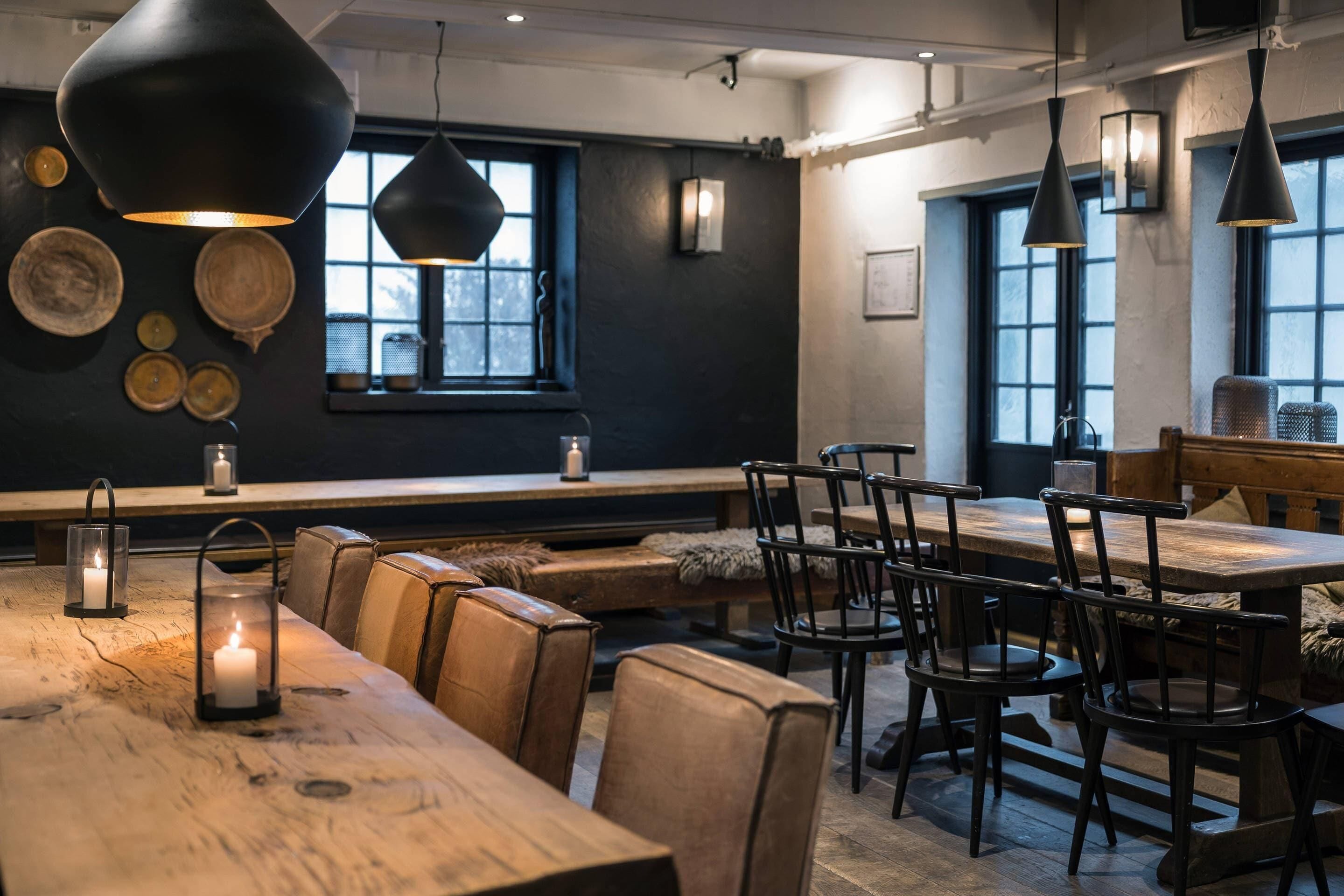 Ein gemütliches Restaurant mit Holztischen und -stühlen, Pendelleuchten und einer Sitzbank an der Wand.