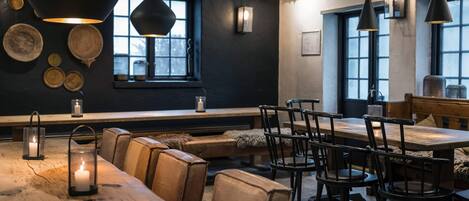 Un restaurante acogedor con mesas y sillas de madera, iluminación colgante y un banco a lo largo de la pared.