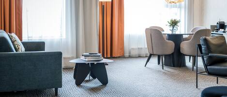 Une chambre d’hôtel moderne avec un canapé, une table basse ronde et un coin repas comprenant des chaises et une table.