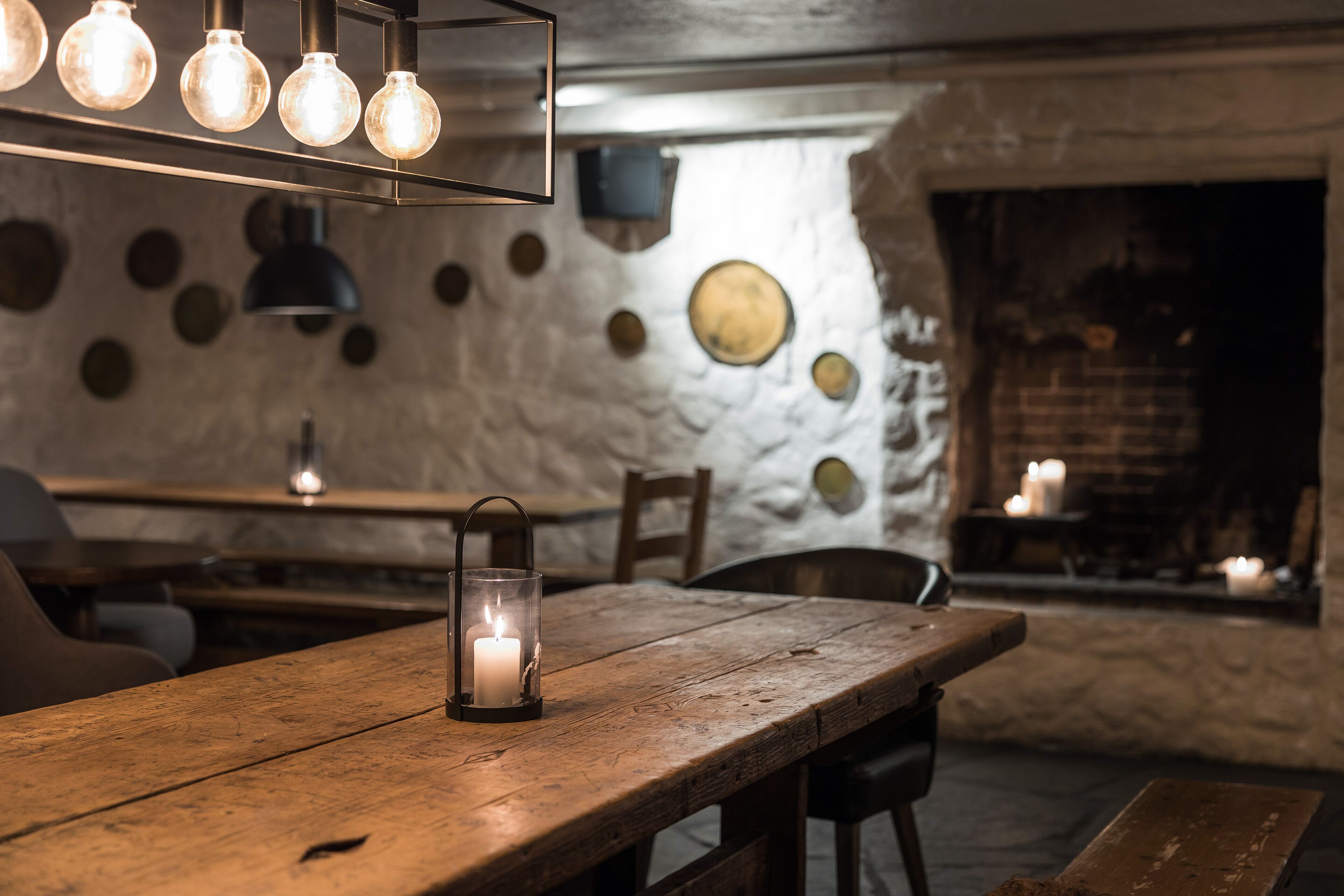 A rustic interior with a wooden table, a lit candle, and a wall adorned with circular decorations.