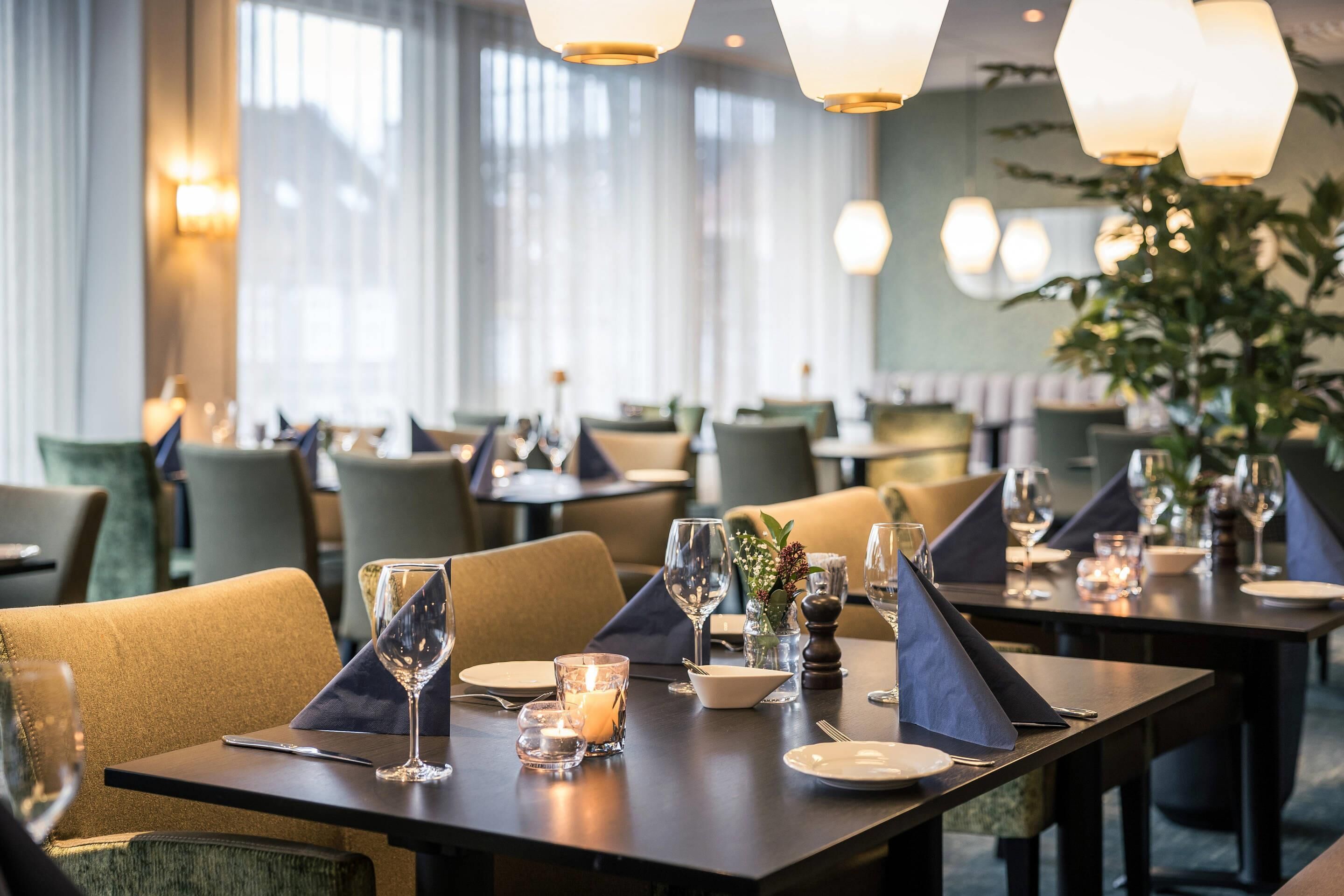 A restaurant with tables set for dining, featuring candle centerpieces and wine glasses.