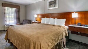Habitación de hotel con una cama grande, dos mesitas de noche con lámparas, una silla, un escritorio y una ventana con cortinas.