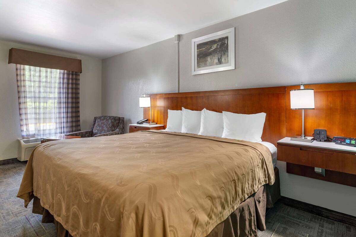 A hotel room with a large bed, two bedside tables with lamps, a chair, a desk, and a window with curtains.