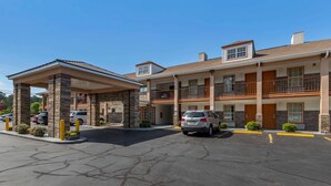 Un hotel de varios pisos con entrada cubierta, estacionamiento exterior y un cielo azul despejado.