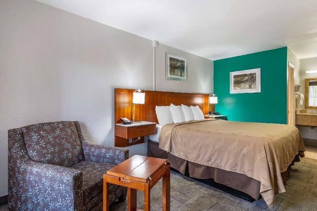 A hotel room with a bed, a chair, a nightstand, and a small table.