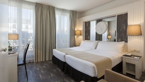 A hotel room with two beds, a desk, a chair, and a large window with curtains. - Hotel Paris Opera Affiliated by Meliá (Paris)