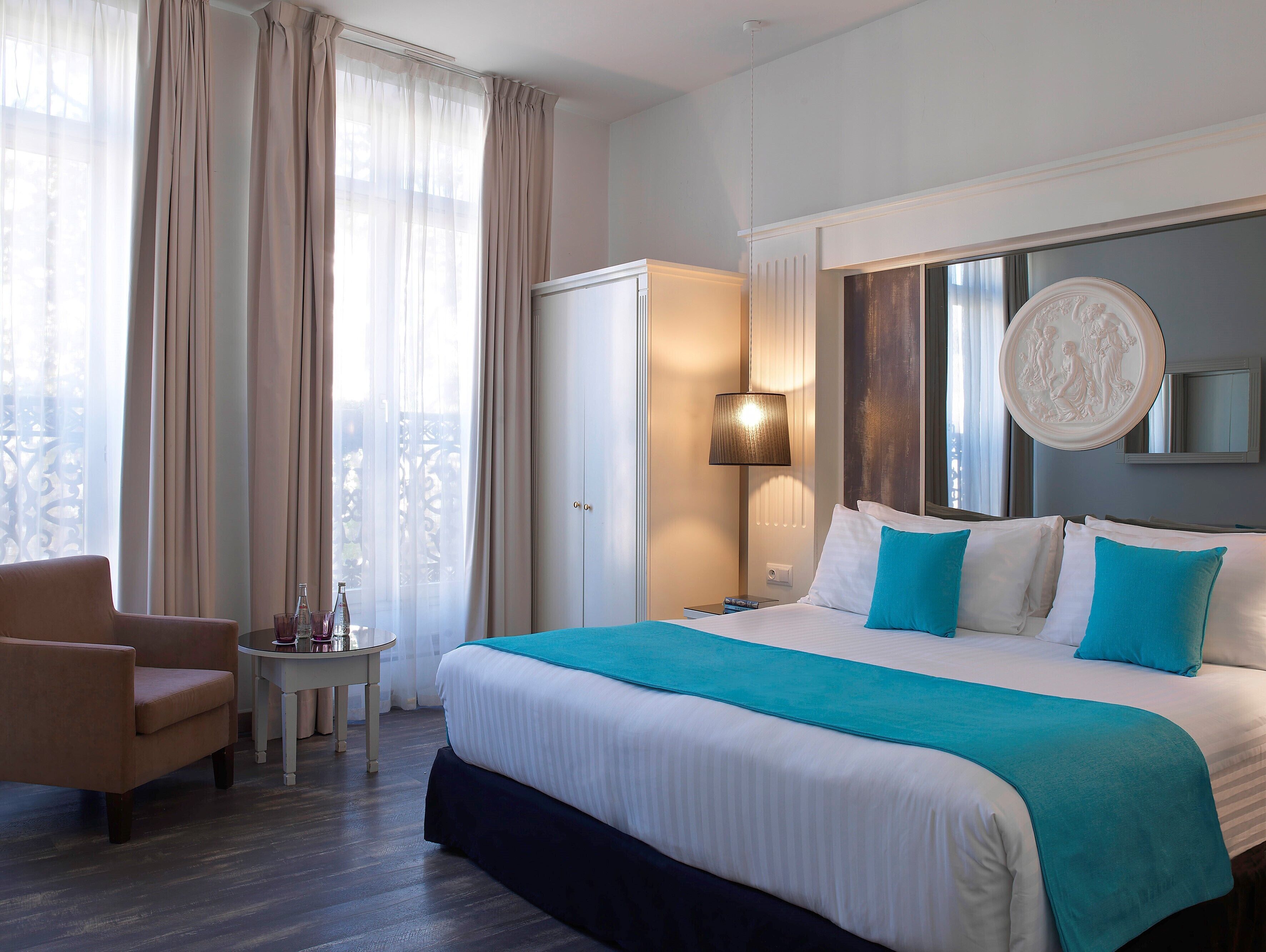 Een hotelkamer met een groot bed, een stoel, een klein tafeltje met een fles en glazen, en een kledingkast.