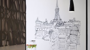 A room with a large black and white cityscape artwork on the wall, a wooden table with potted plants, and a yellow armchair. - Hotel Paris Opera Affiliated by Meliá (Paris)