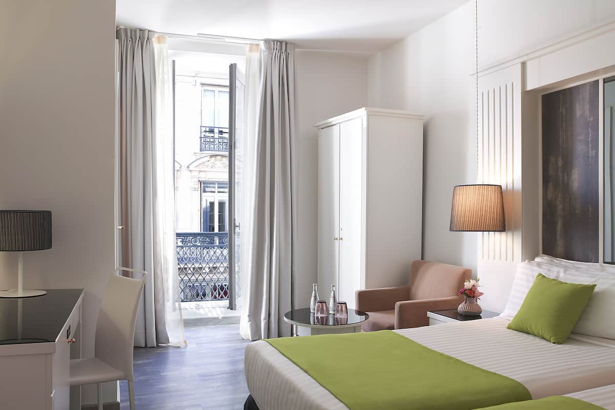 A hotel room with two beds, a desk, a chair, a wardrobe, and a balcony with a view.