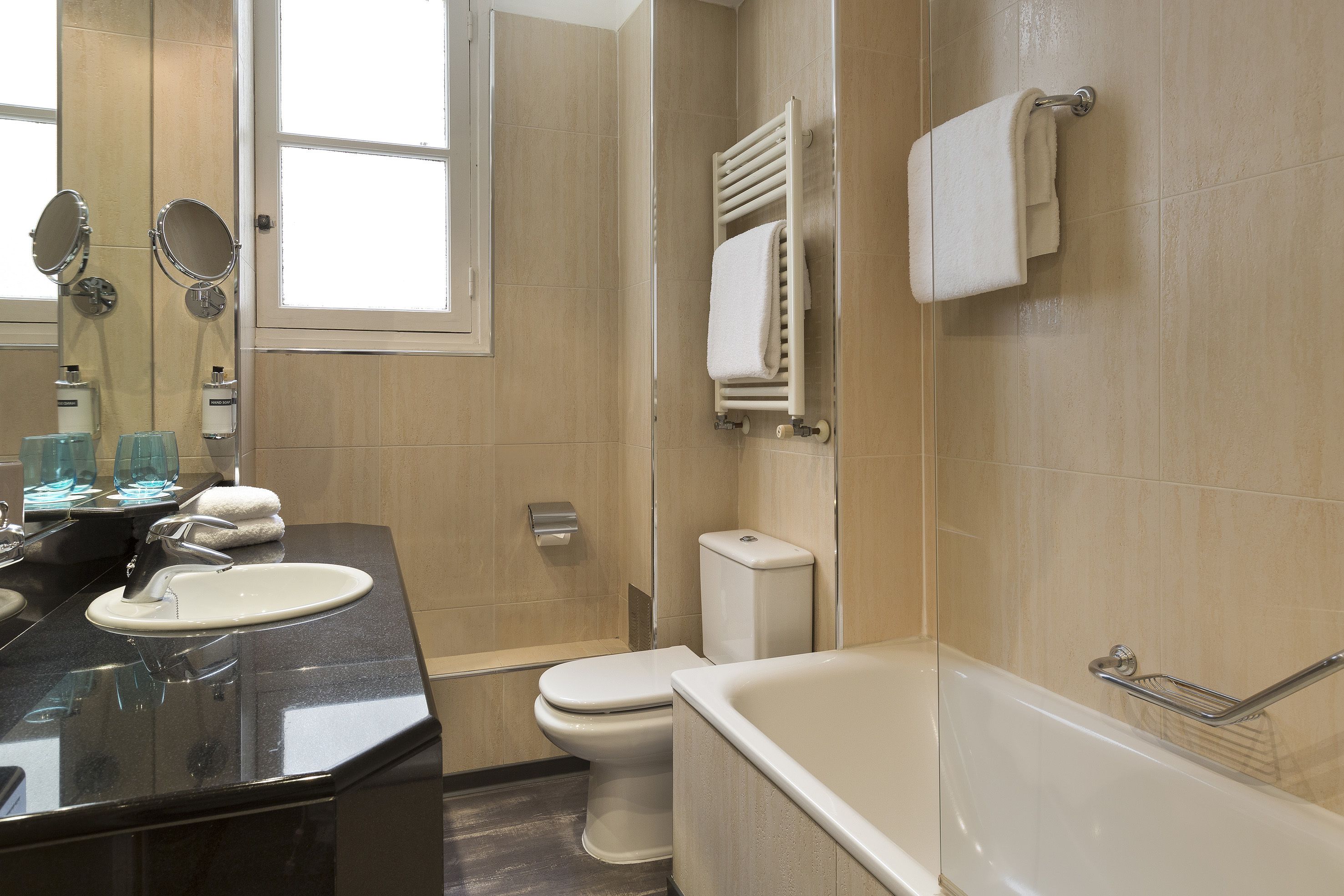 A modern bathroom with a black sink, two mirrors, a toilet, and a bathtub.