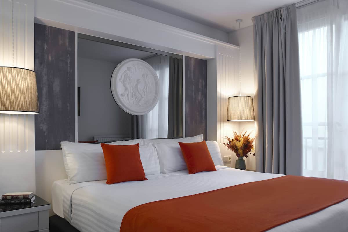 A modern hotel room with a large bed, two pillows, a bedside table with a book, and a vase with flowers.