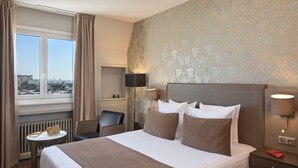 A hotel room with a large bed, a desk, a chair, and a view of the city through a window. - Timhotel Opera Blanche Fontaine (Paris)