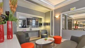 A modern lounge area with a round table, comfortable seating, and decorative plants. - Timhotel Opera Blanche Fontaine (Paris)
