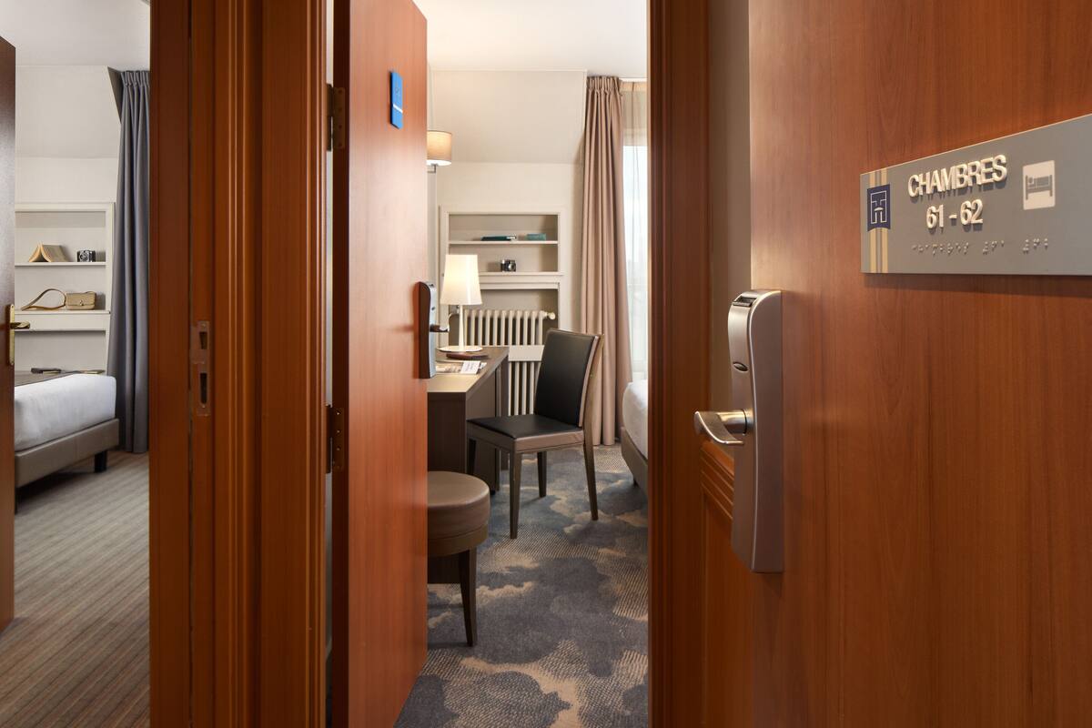 Habitación de hotel con cama, escritorio, silla, lámpara y un cartel que indica el número de habitación 61-62.