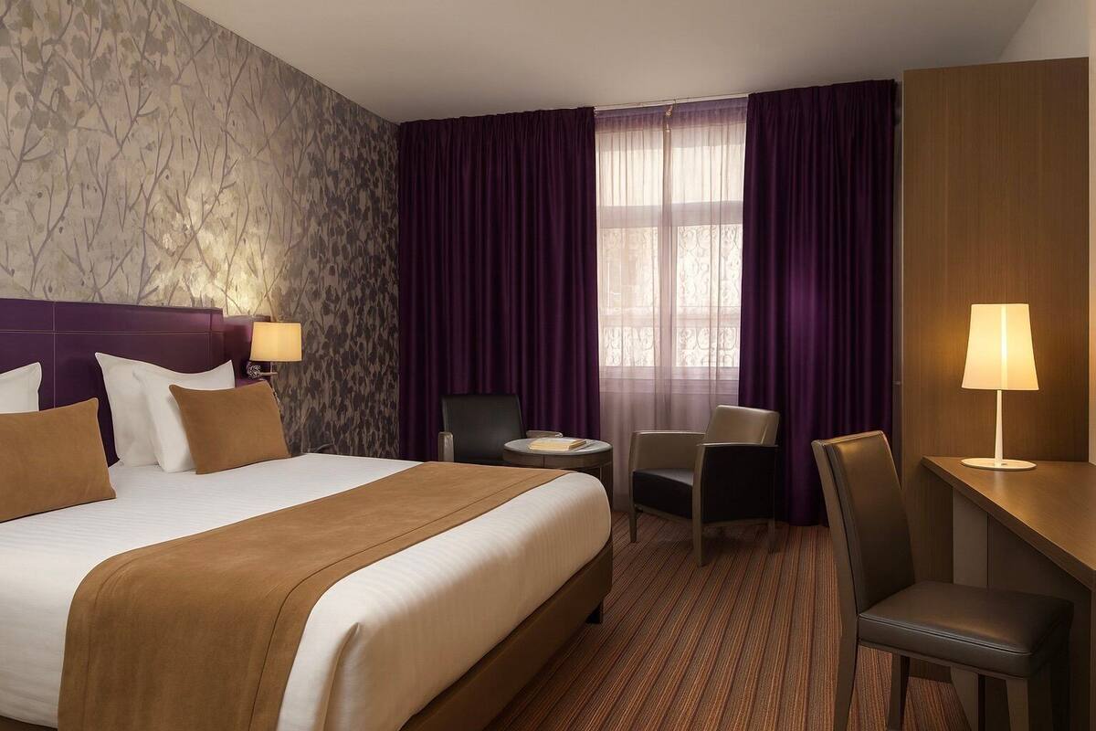Una habitación de hotel con una cama grande, dos sillas, un escritorio y una lámpara.