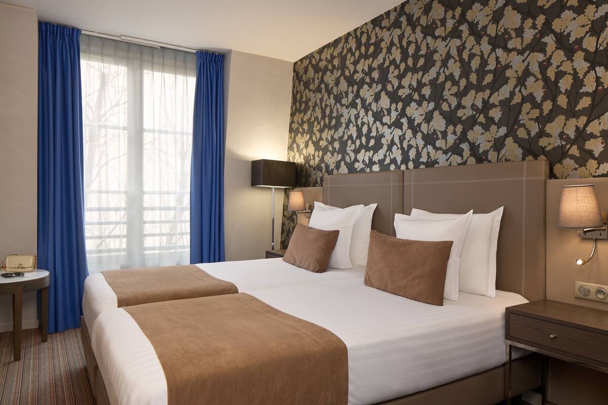 Habitación de hotel con una cama grande, dos mesitas de noche, una lámpara y un papel tapiz estampado.