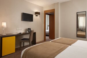 A hotel room with a bed, desk, chair, and a television.