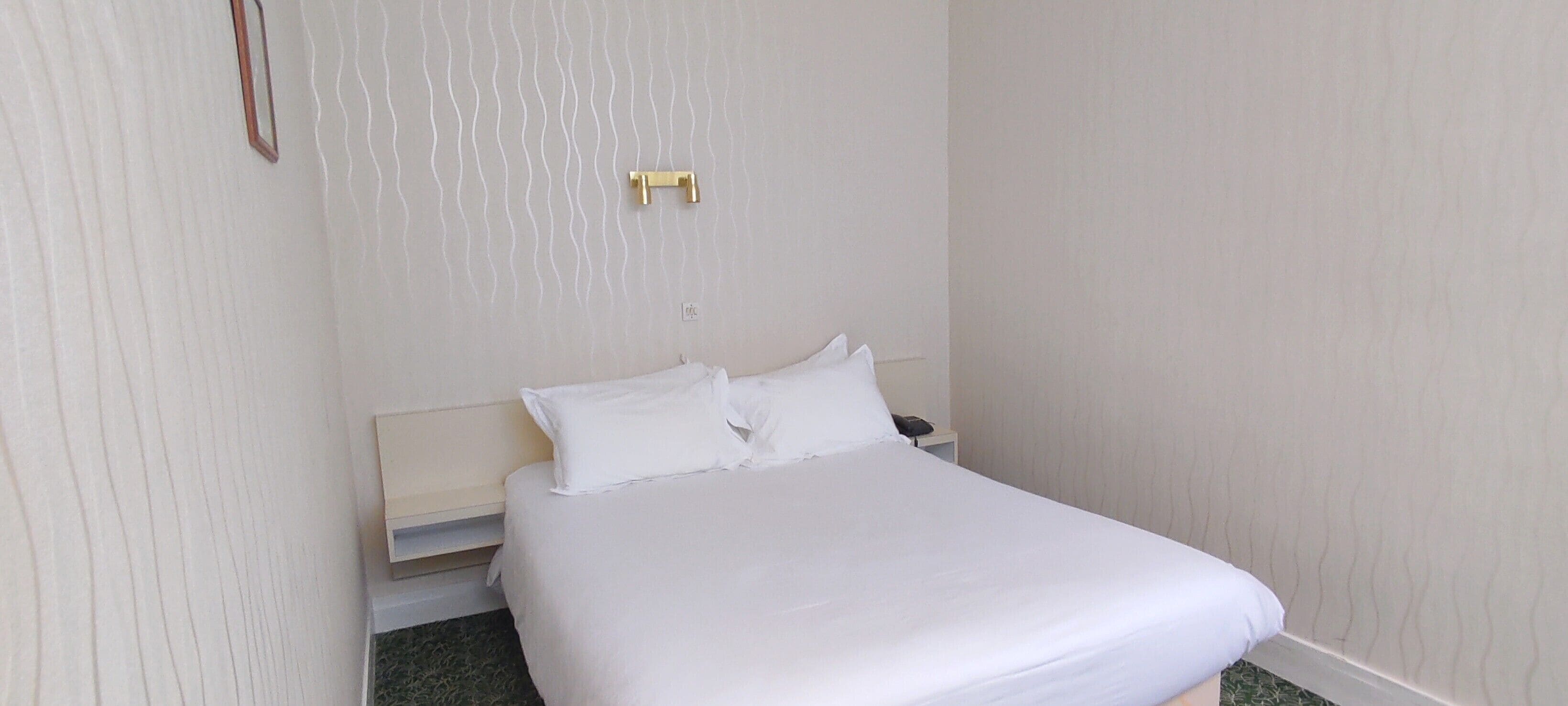 Una cama bien tendida con sábanas blancas y dos almohadas en una habitación con paredes de colores claros y un cabecero de madera.