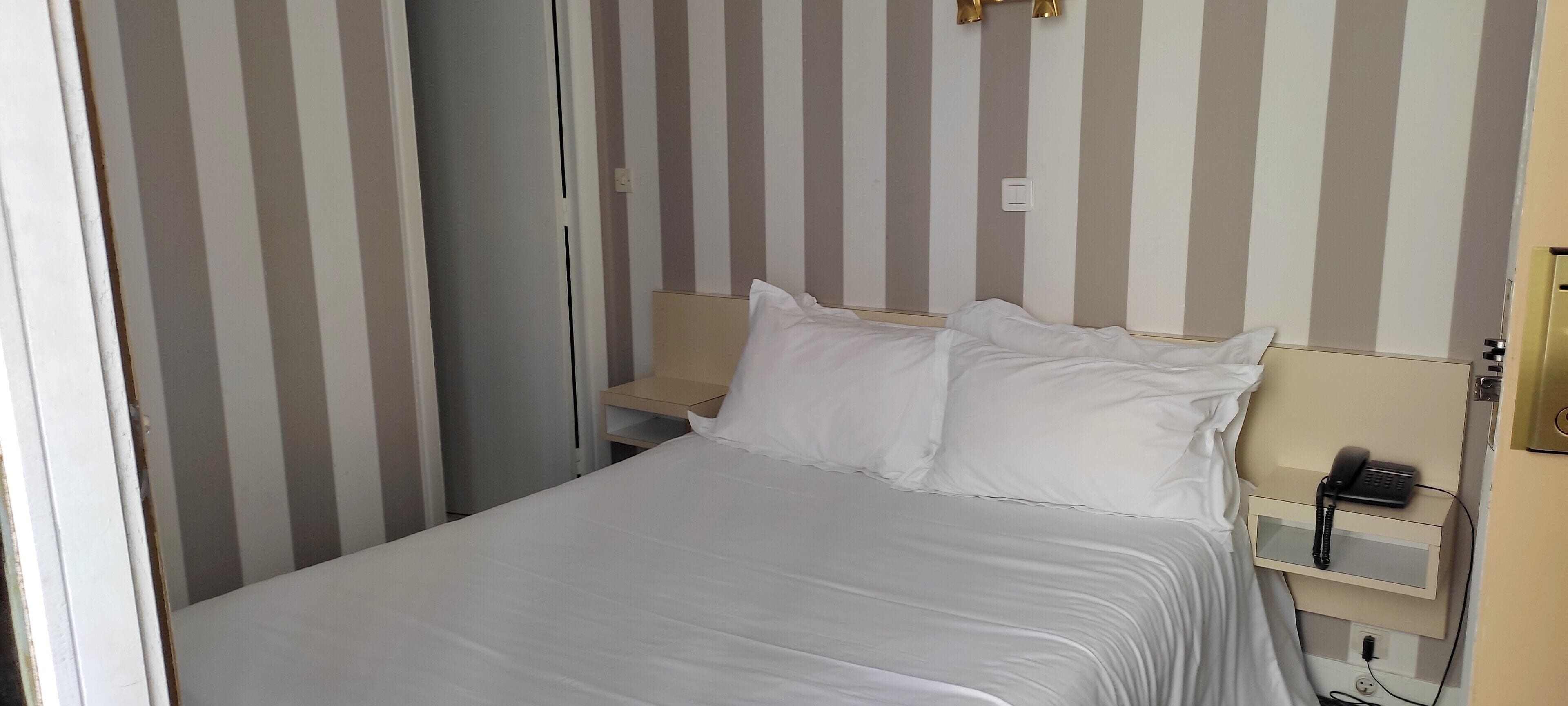 A hotel room with a bed, a bedside table with a phone, and a striped wall.