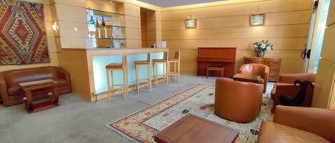 A cozy living room with a bar area, leather sofas, a piano, and a patterned rug.