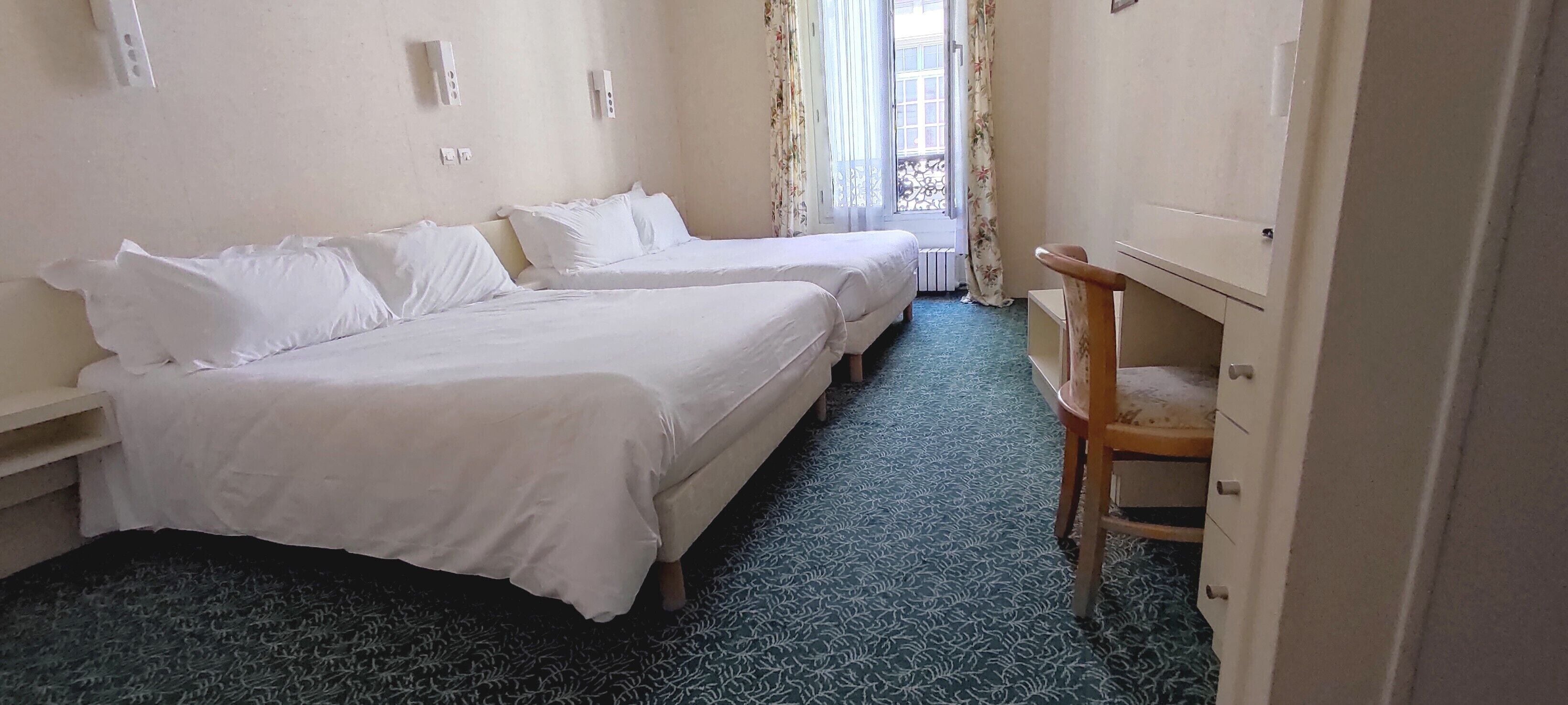 A hotel room with two beds, a wooden chair, and a window with curtains.