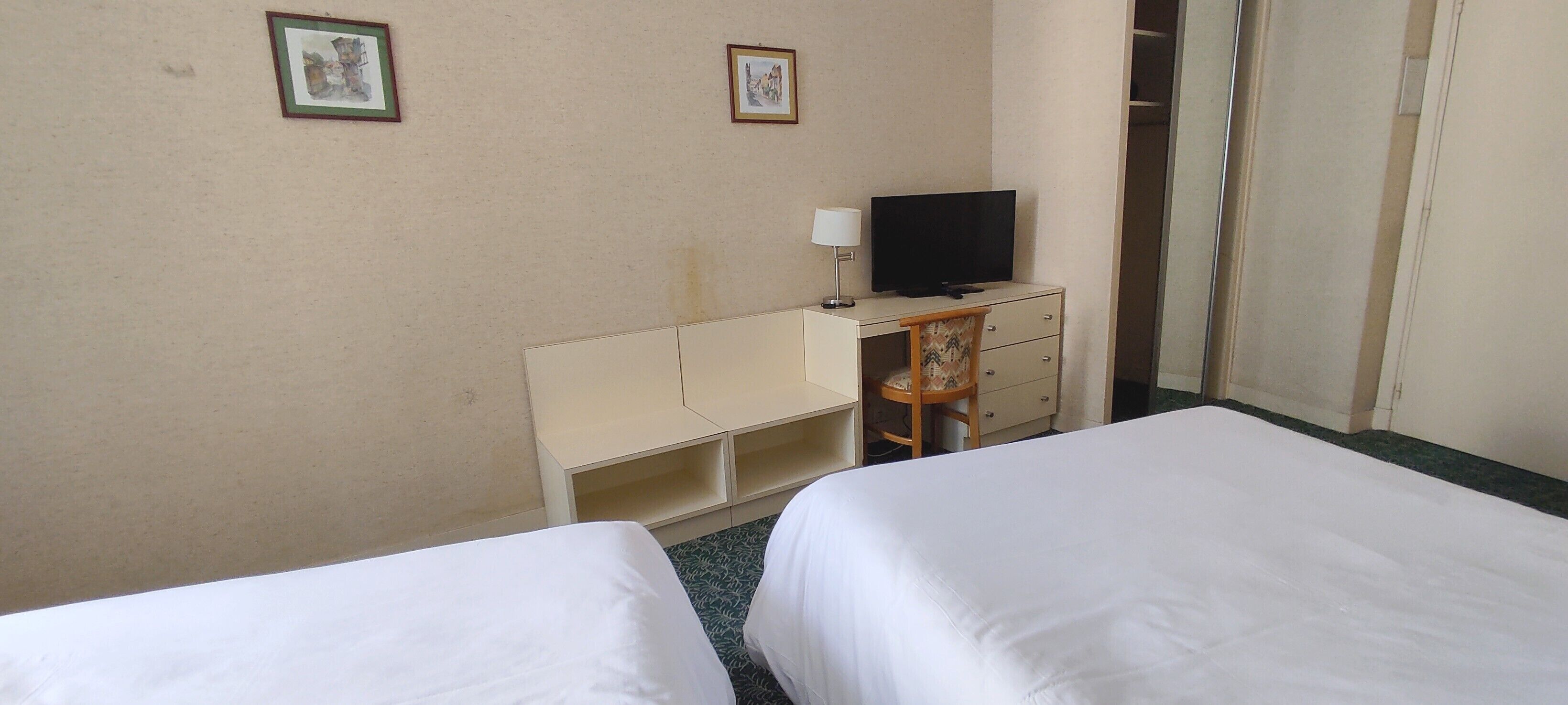 Una habitación de hotel con dos camas, un escritorio con televisor y un armario.