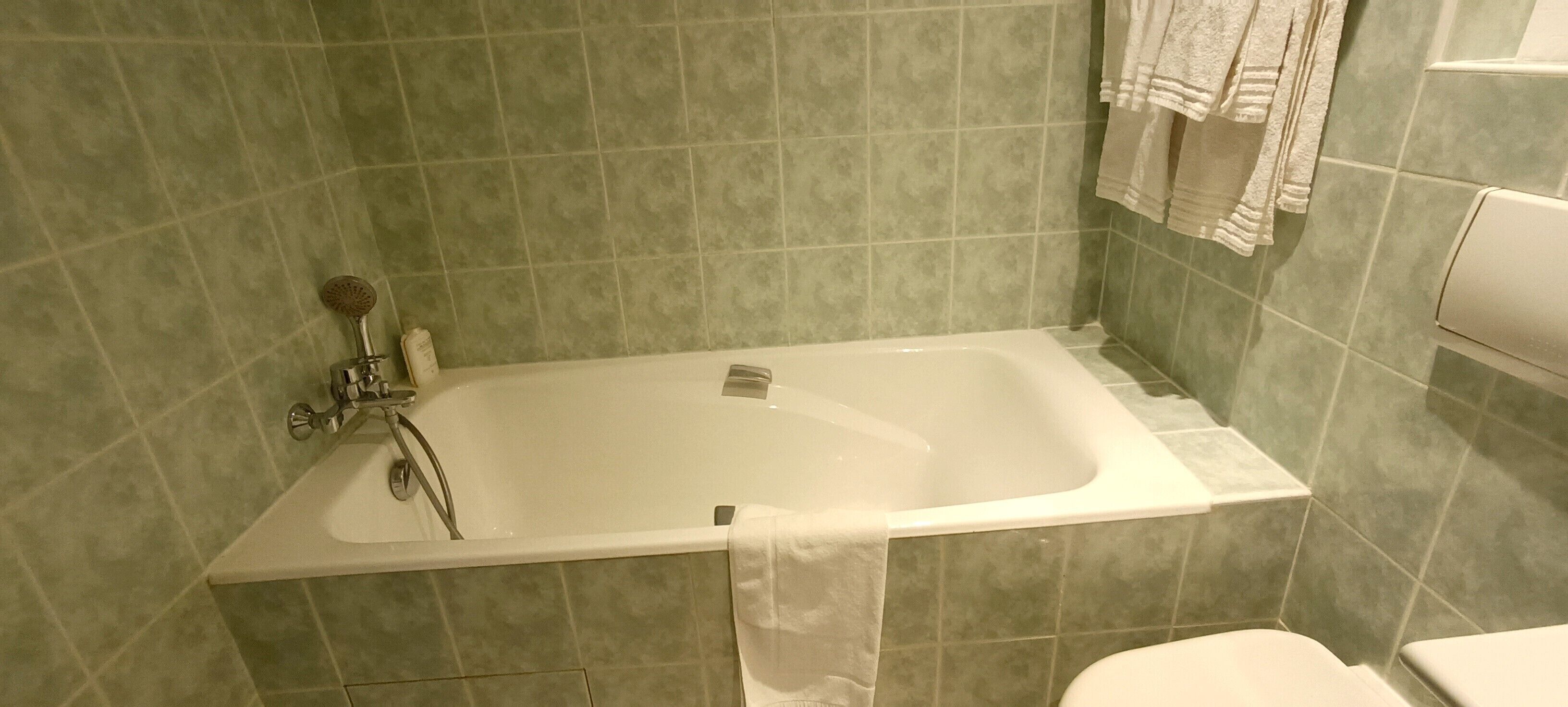 Een badkamer met een bad, toilet en een handdoekrek met handdoeken.