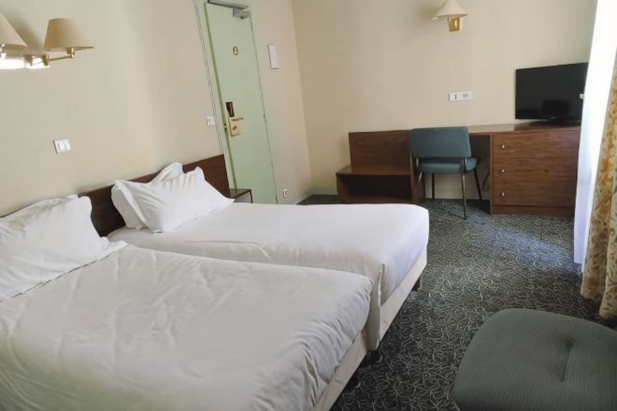 A hotel room with two beds, a desk, a chair, a television, and a door.