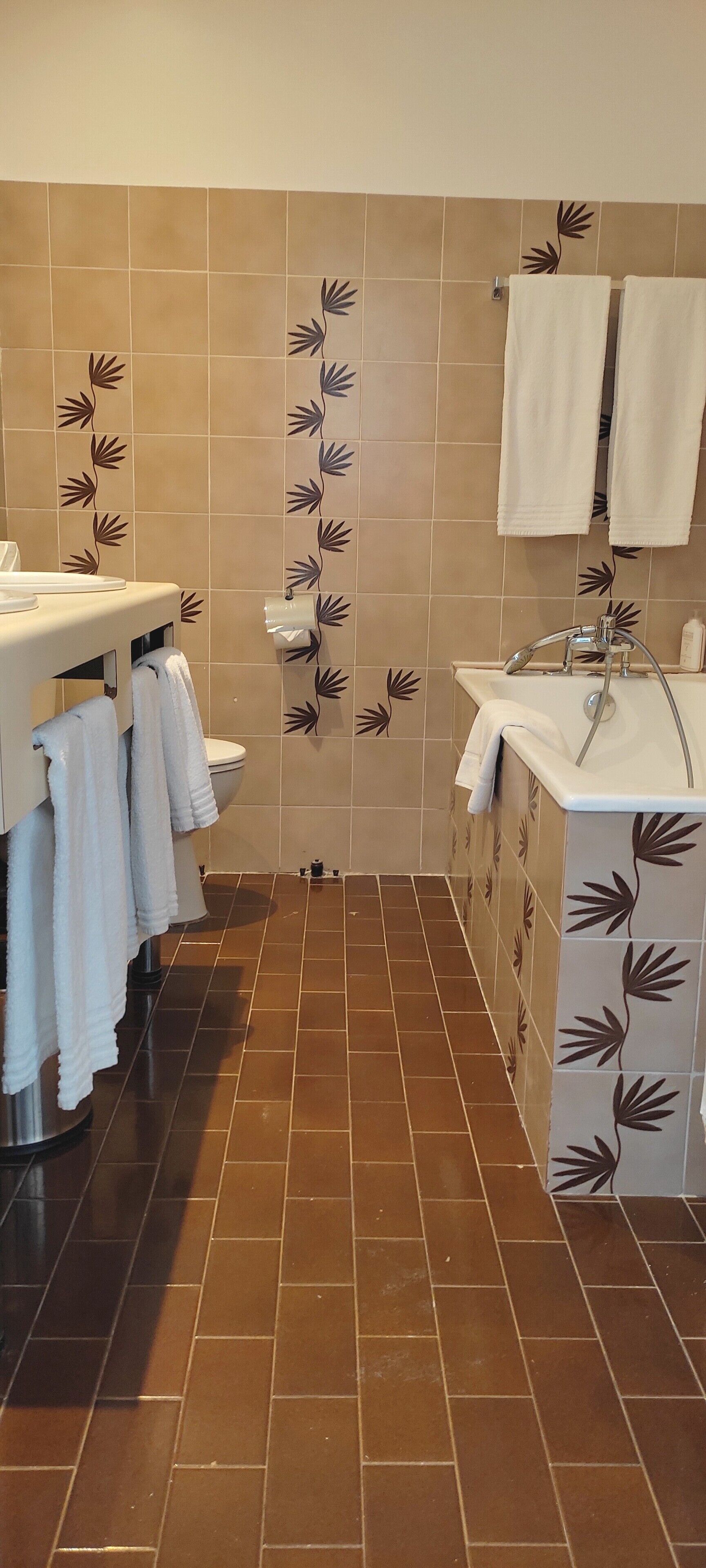 A bathroom with a toilet, sink, and bathtub. There are towels hanging on the wall and a toilet paper holder.