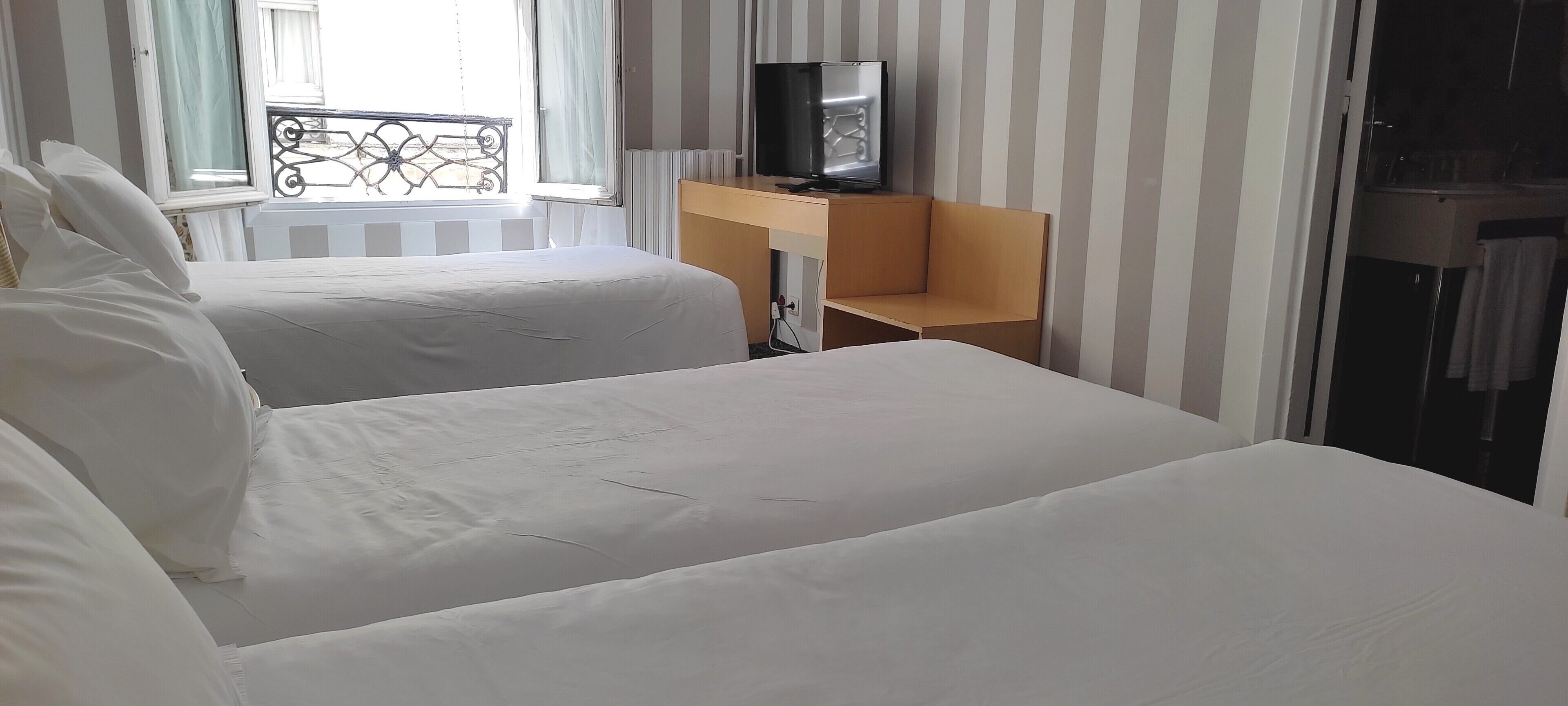 A hotel room with two beds, a TV on a wooden desk, and a window with a view of the outside balcony.