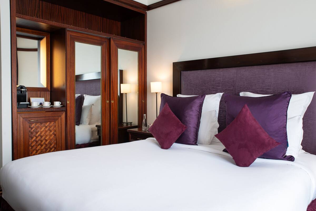 A hotel room with a large bed, wooden wardrobe, and a nightstand with a lamp.