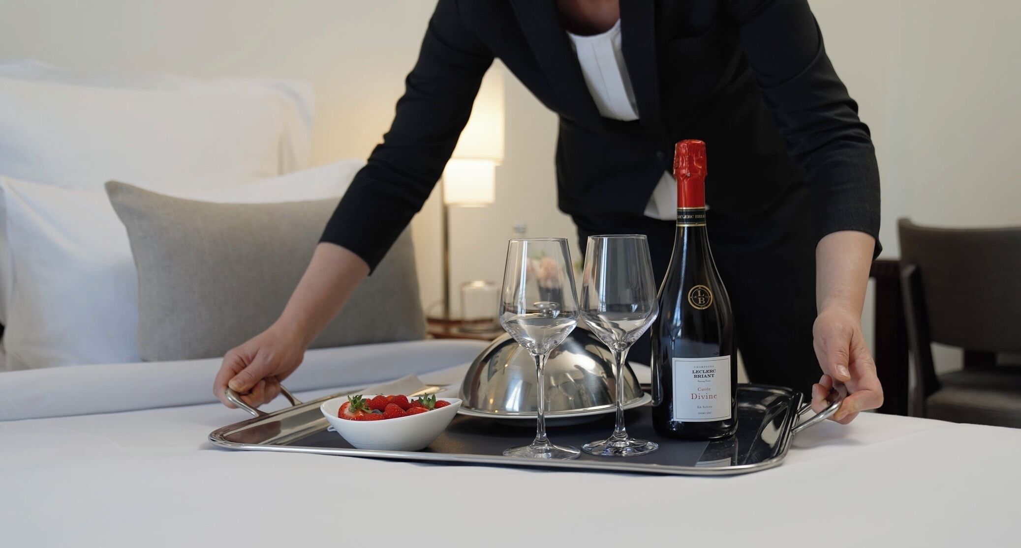 A tray with a bottle of champagne, two wine glasses, and a bowl of strawberries on a hotel bed.