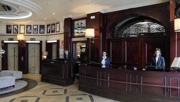 Zona de recepción con un imponente mostrador de madera, dos recepcionistas y un arco decorativo.