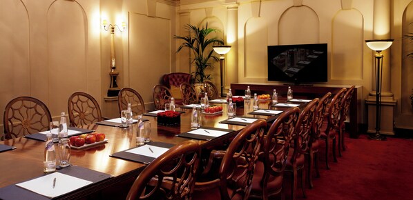 A conference room with a long table, chairs, a television, and a potted plant.