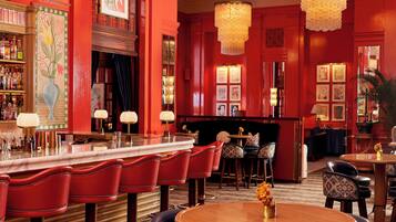 A bar area with red upholstered bar stools, a marble counter, and a patterned vase on a round table.